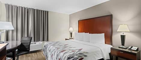 A hotel room with a bed, desk, chair, and a desk lamp.