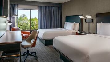 A hotel room with two beds, a desk, a chair, and a large window with curtains.