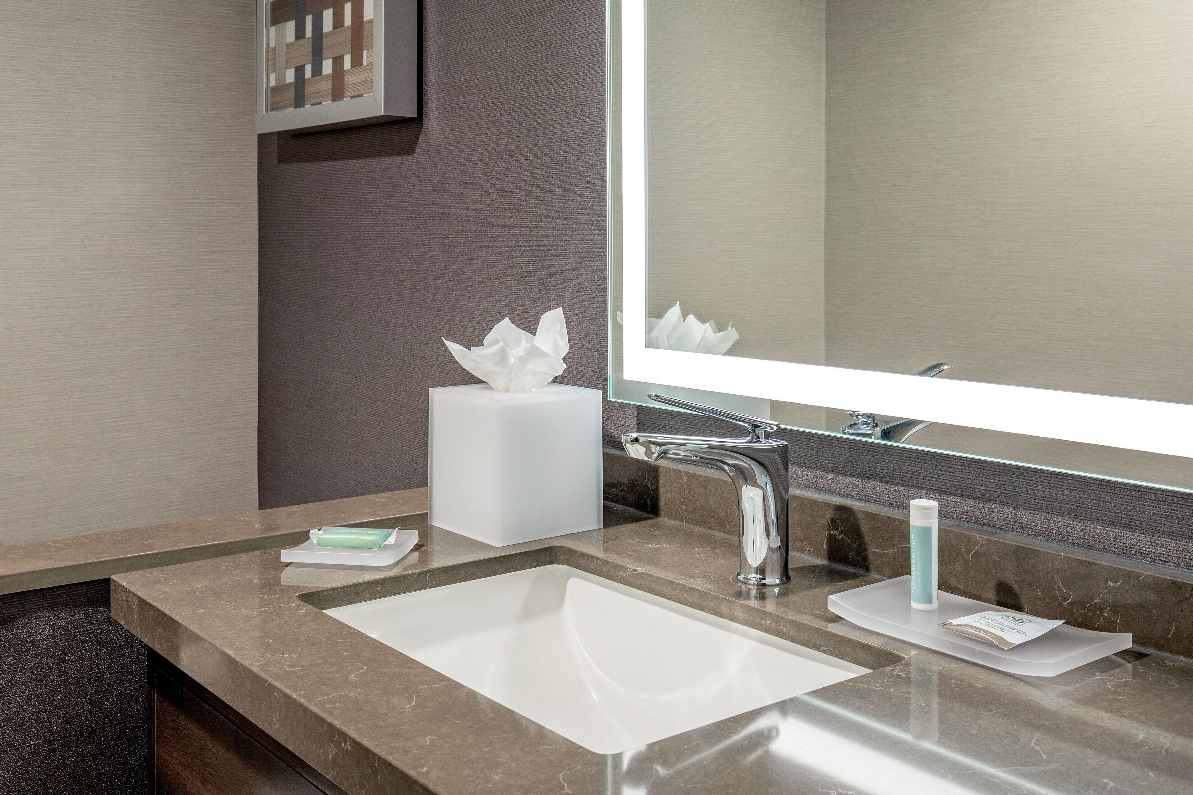 A modern bathroom with a large mirror, a sink, and a towel dispenser.