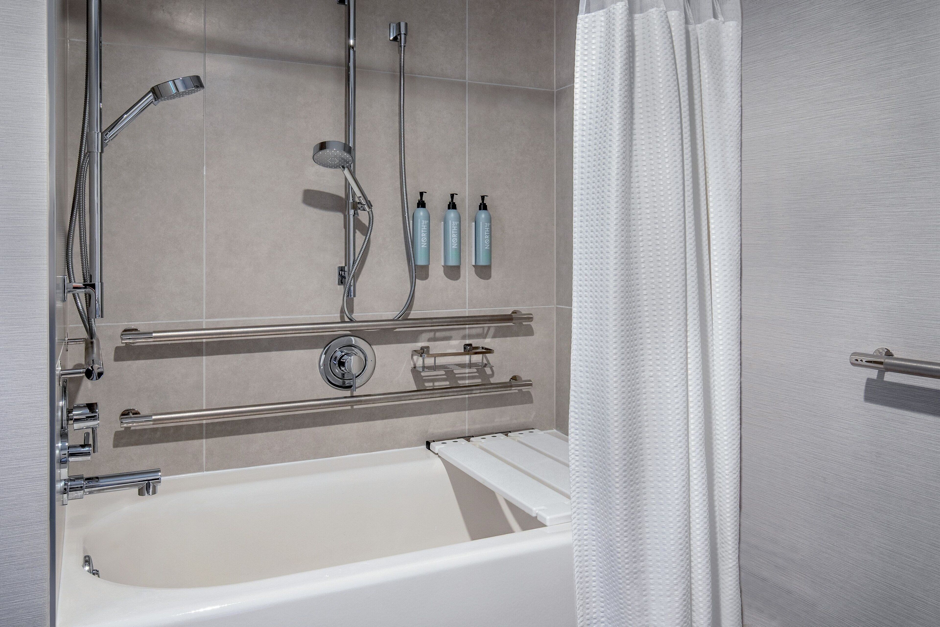 A modern bathroom with a bathtub, a shower with a handheld showerhead, and two bottles of lotion on a shelf.