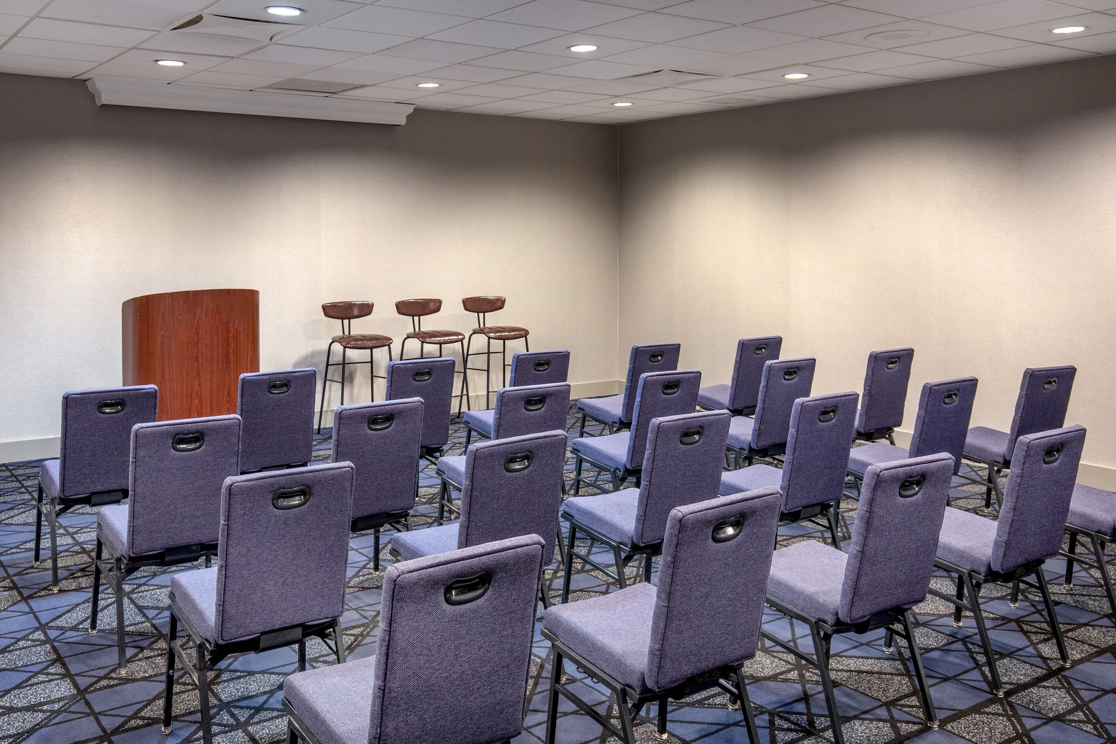 A conference room with rows of purple chairs, a wooden podium, and a patterned carpet.