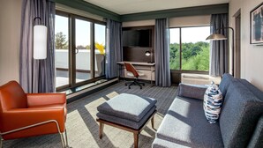 A modern hotel room with a sofa, armchair, ottoman, desk, and TV. - Courtyard by Marriott Boston Marlborough (Marlborough)