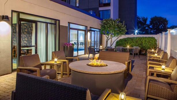 An outdoor patio with wicker furniture, a central fire pit, and tables with candles. - Courtyard by Marriott Boston Marlborough (Marlborough)