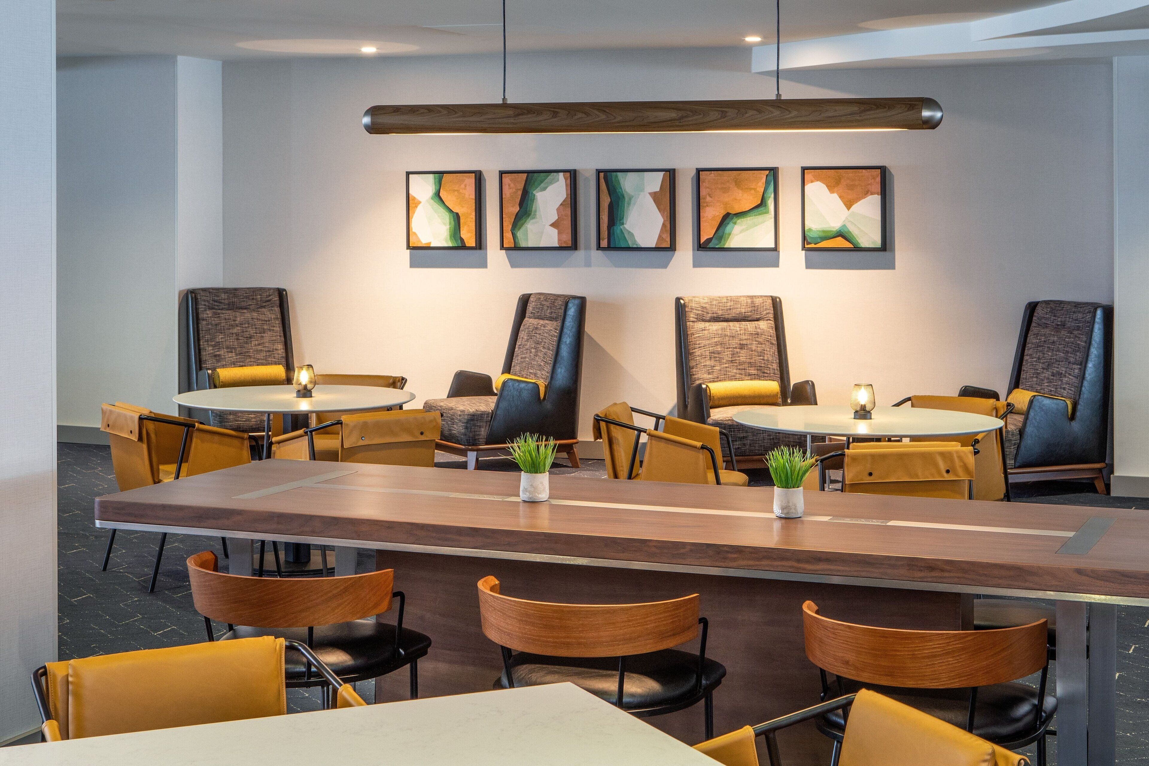 Un espace repas moderne avec des tables rondes et des chaises jaunes, agrémenté d’œuvres d’art abstraites au mur et d’une table centrale en bois.