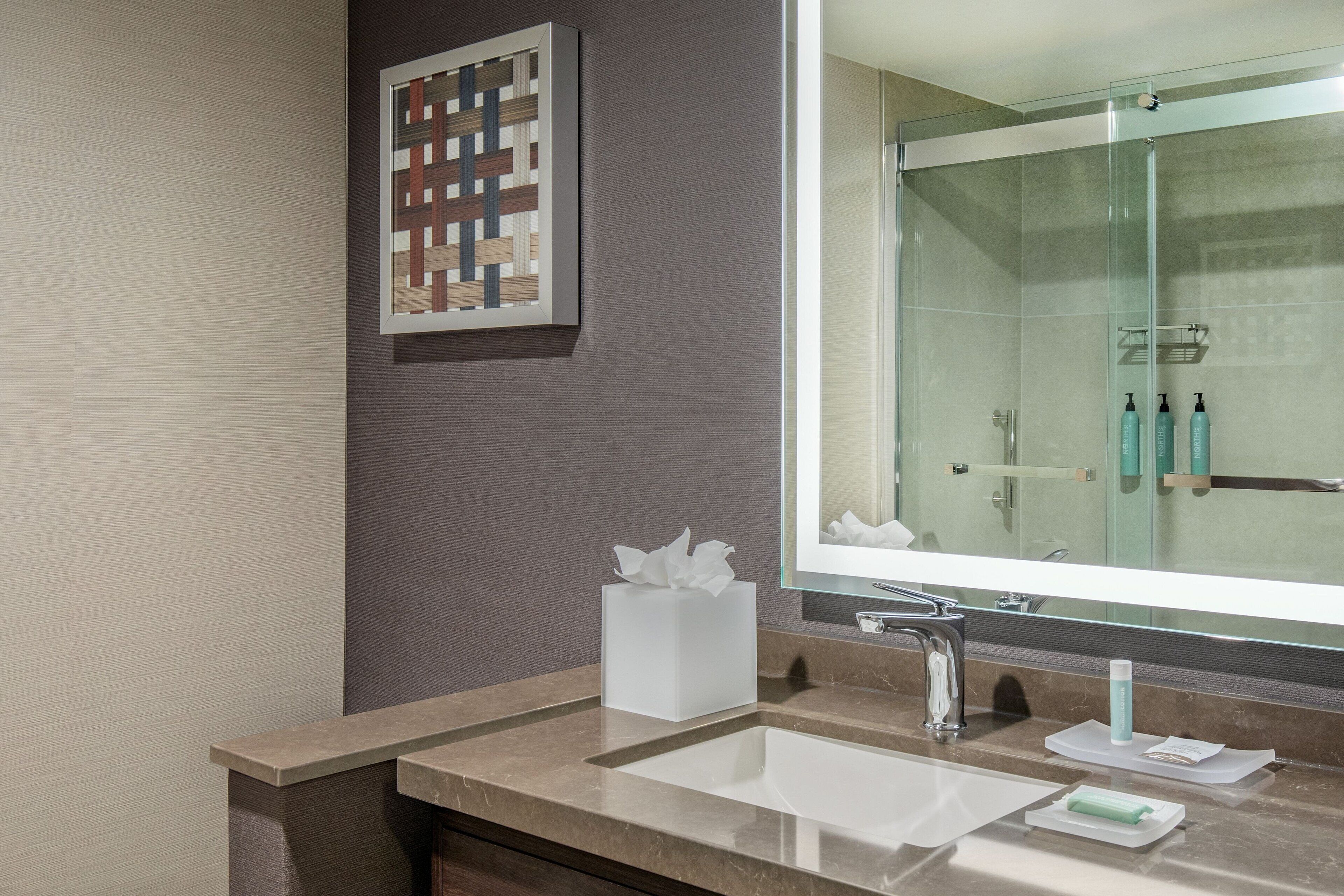 A modern bathroom with a large mirror, a sink, and a glass shower enclosure.