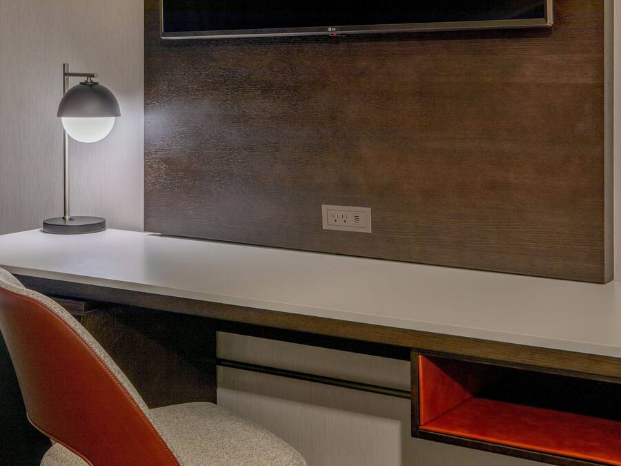 A modern office desk with a lamp, a chair, and a TV mounted on the wall.