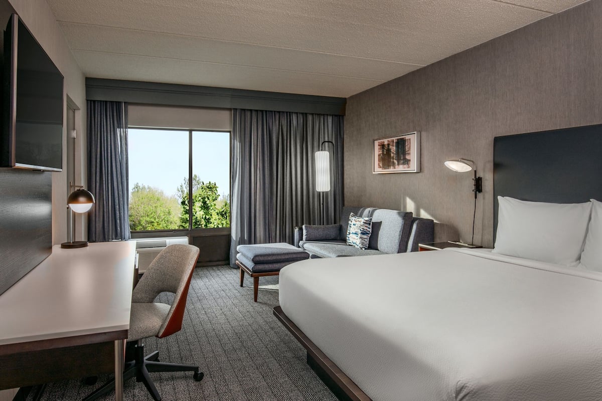 A hotel room with a large bed, a desk with a chair, a sofa, and a TV.