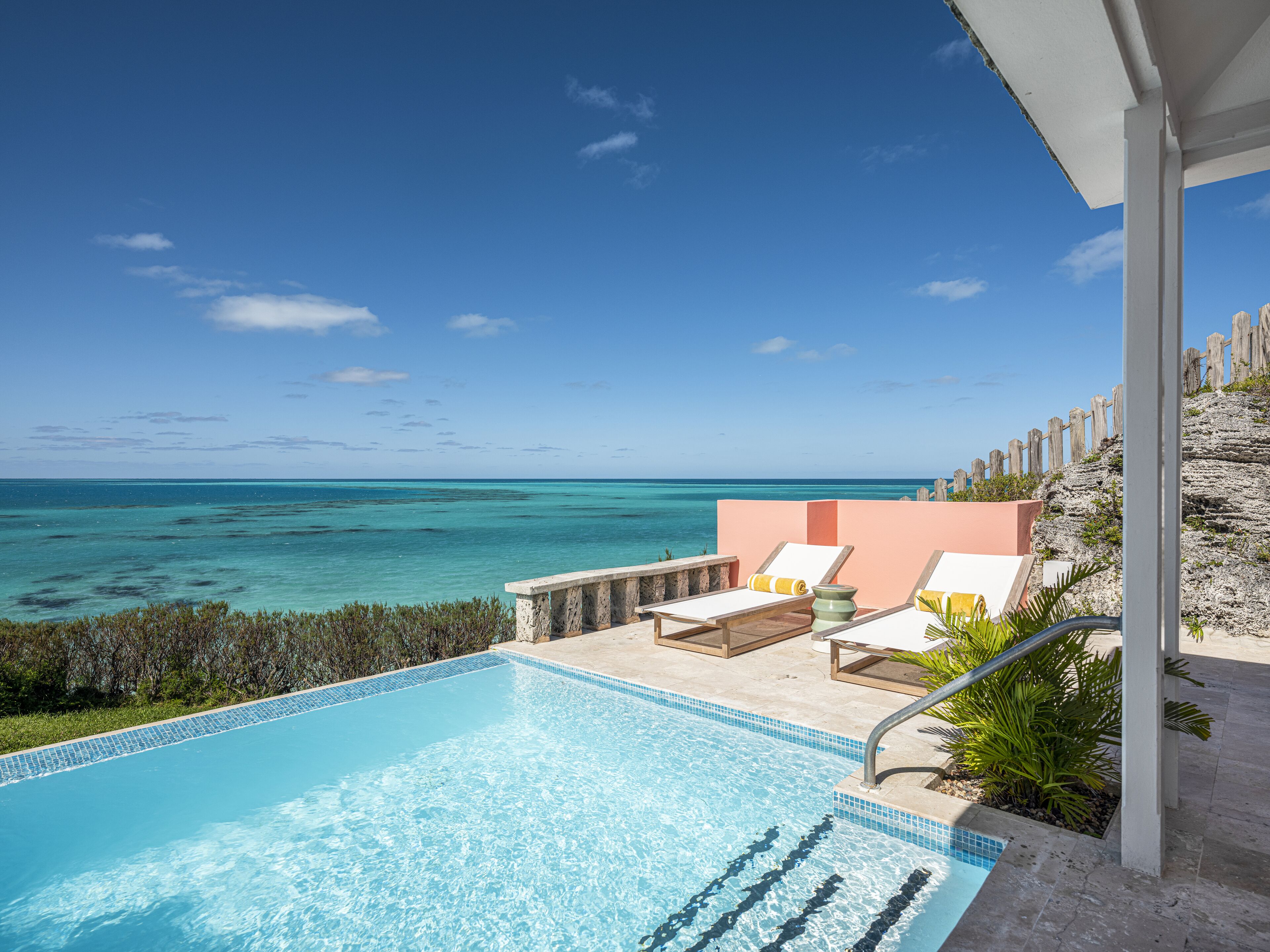 A pool with clear blue water, surrounded by lounge chairs and a view of the ocean.