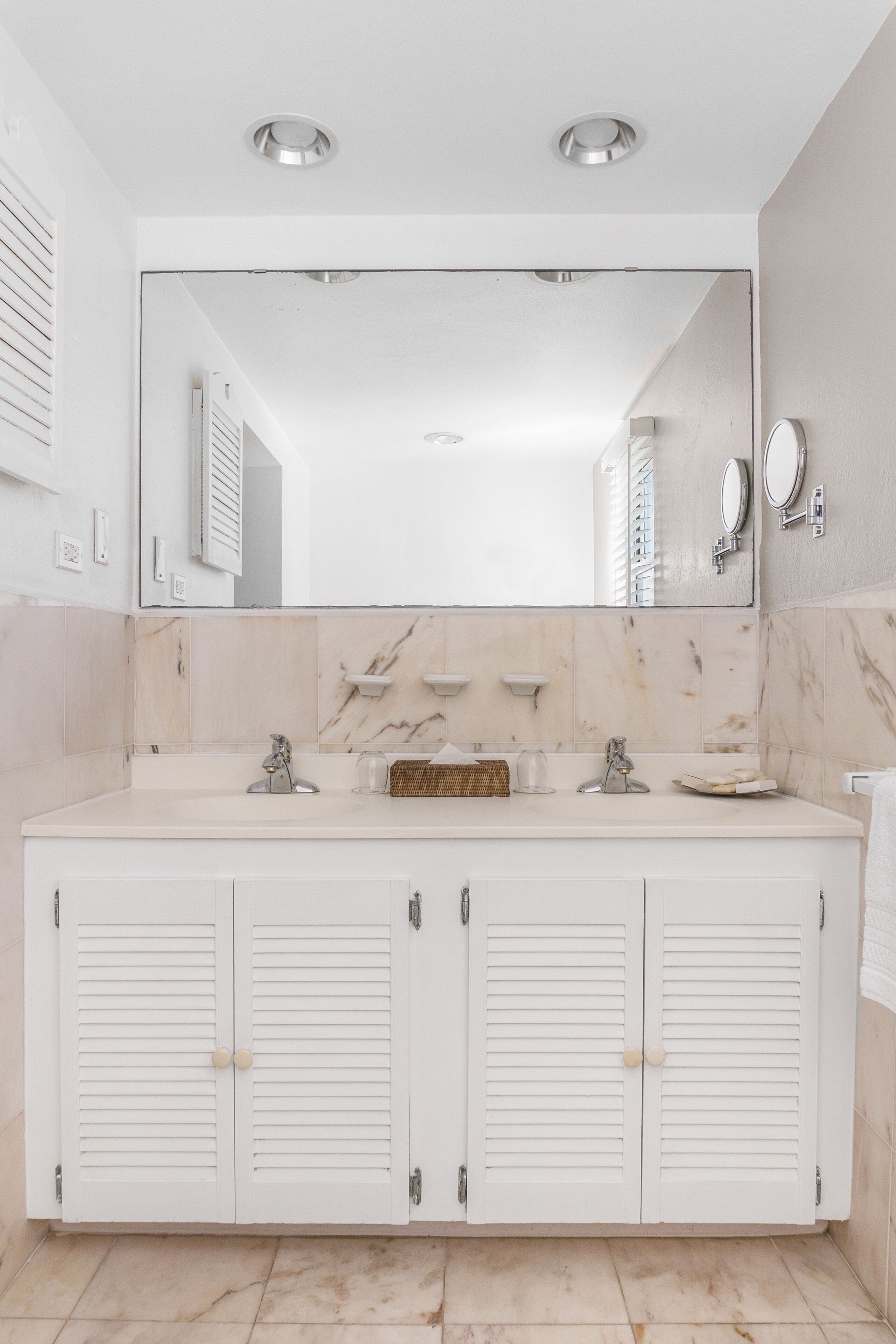 Une salle de bain avec un grand miroir, deux lavabos et des placards.