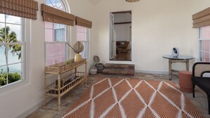 A room with large windows, a wicker side table, a patterned rug, and a ceiling light fixture.