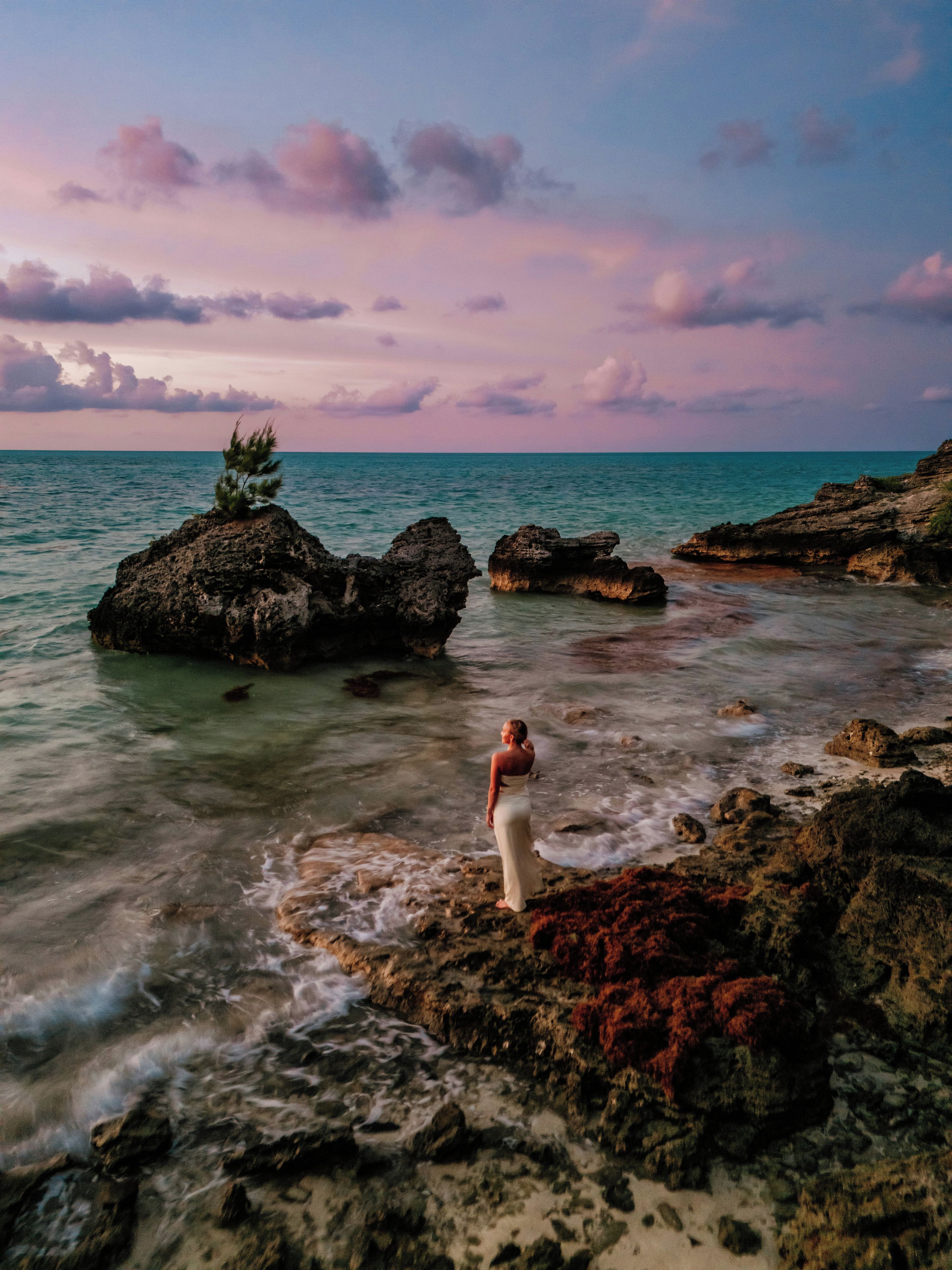 A rocky shoreline with clear water and a person standing on the rocks.