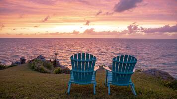 Two Adirondack chairs facing a sunset over the ocean.
