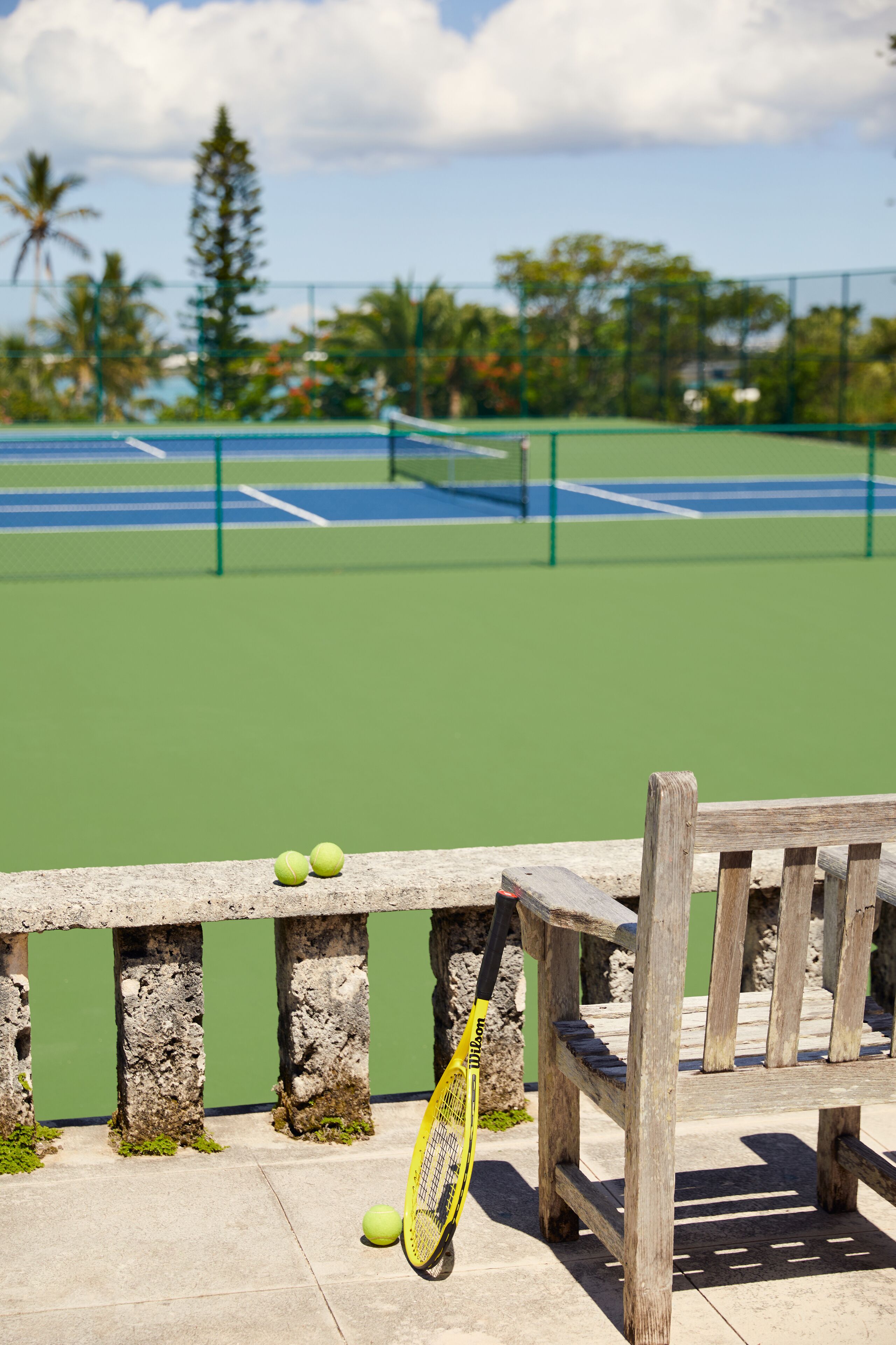 A tennis court with a bench and tennis balls.