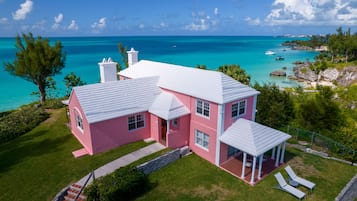 Een roze huis met een wit dak, een overdekte veranda en uitzicht op de oceaan.