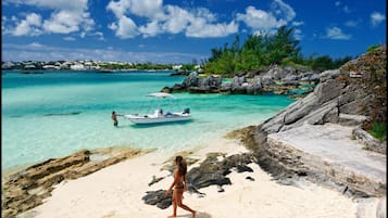 Een strand met helder turquoise water, een rotsachtige kustlijn en een boot die daar ligt ankeren.
