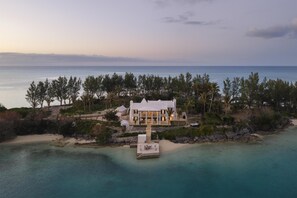 A large, white, multi-story house with a dock extending into a turquoise sea, surrounded by dense greenery and a clear sky. - Cambridge Beaches Resort & Spa (Sandys Parish)