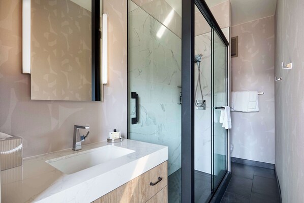 Une salle de bain moderne avec un grand miroir, un lavabo blanc et une cabine de douche en verre.