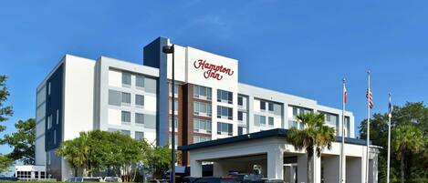 Un hotel Hampton Inn con un diseño moderno, que cuenta con un cartel llamativo, una zona de estacionamiento techada y un césped bien cuidado.