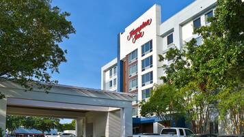 A hotel with a 'Welcome' sign, a parking lot with several vehicles, and a clear blue sky.