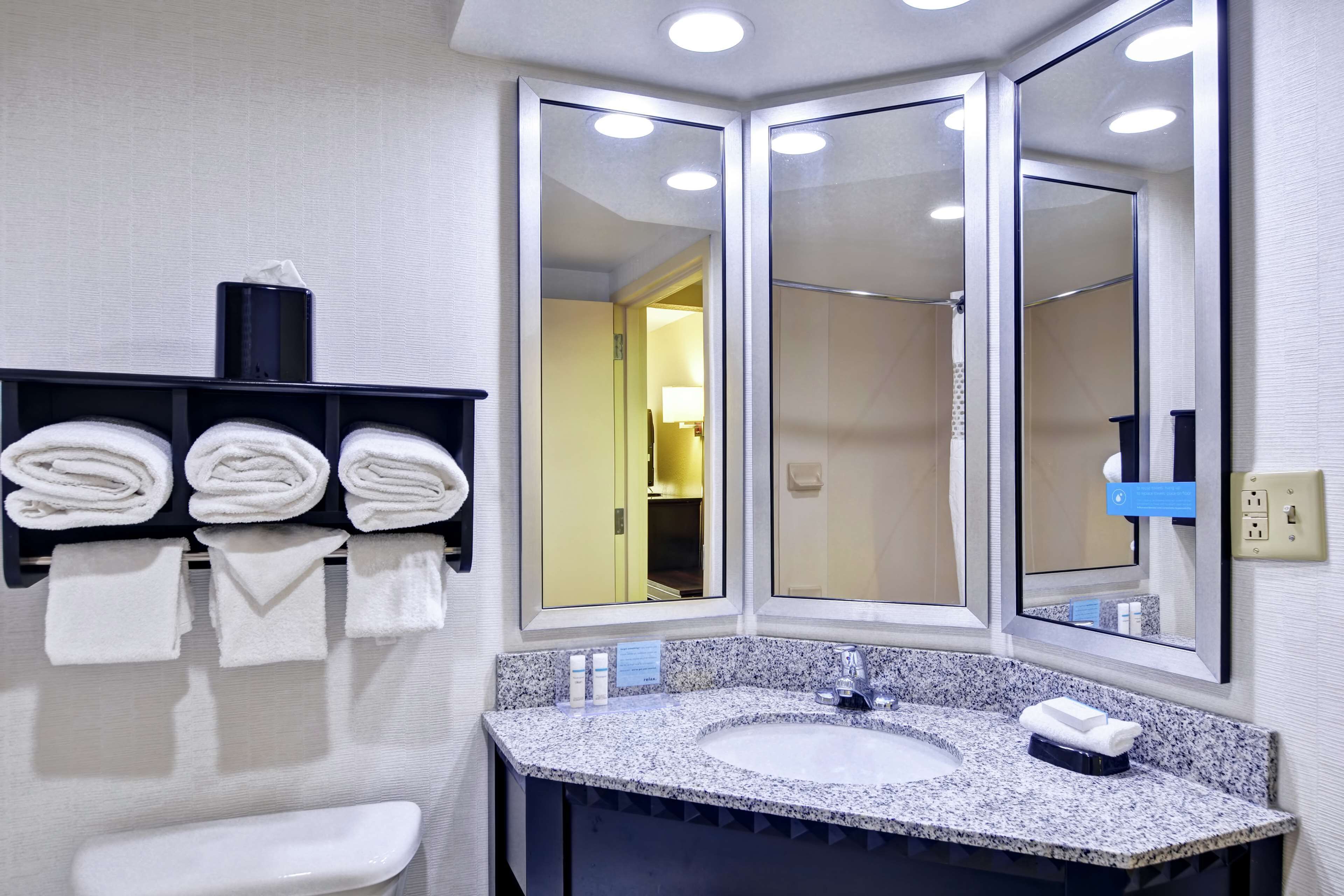 A modern bathroom with a granite countertop sink, a large mirror, and a towel rack with neatly folded towels.