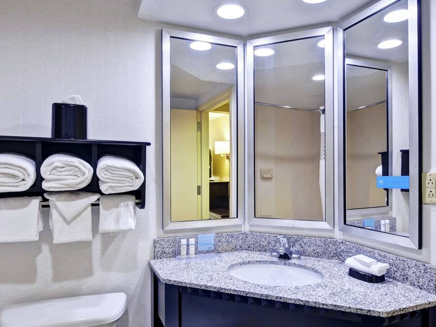 A modern bathroom with a granite countertop sink, a large mirror, and a towel rack with neatly folded towels.