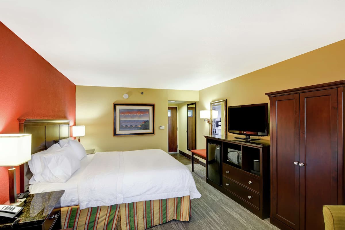 A hotel room with a bed, bedside lamps, a television, a dresser, and a framed picture on the wall.
