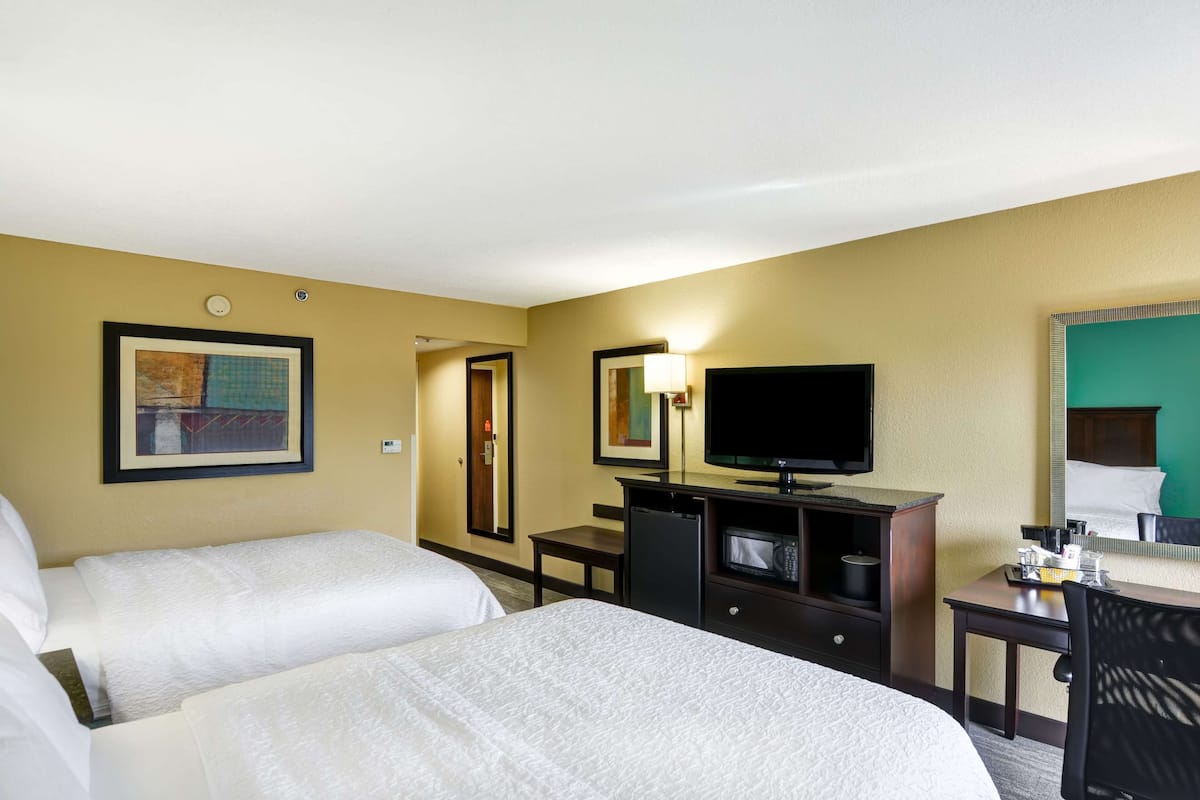 A hotel room with two beds, a television, a desk with a chair, and a microwave.