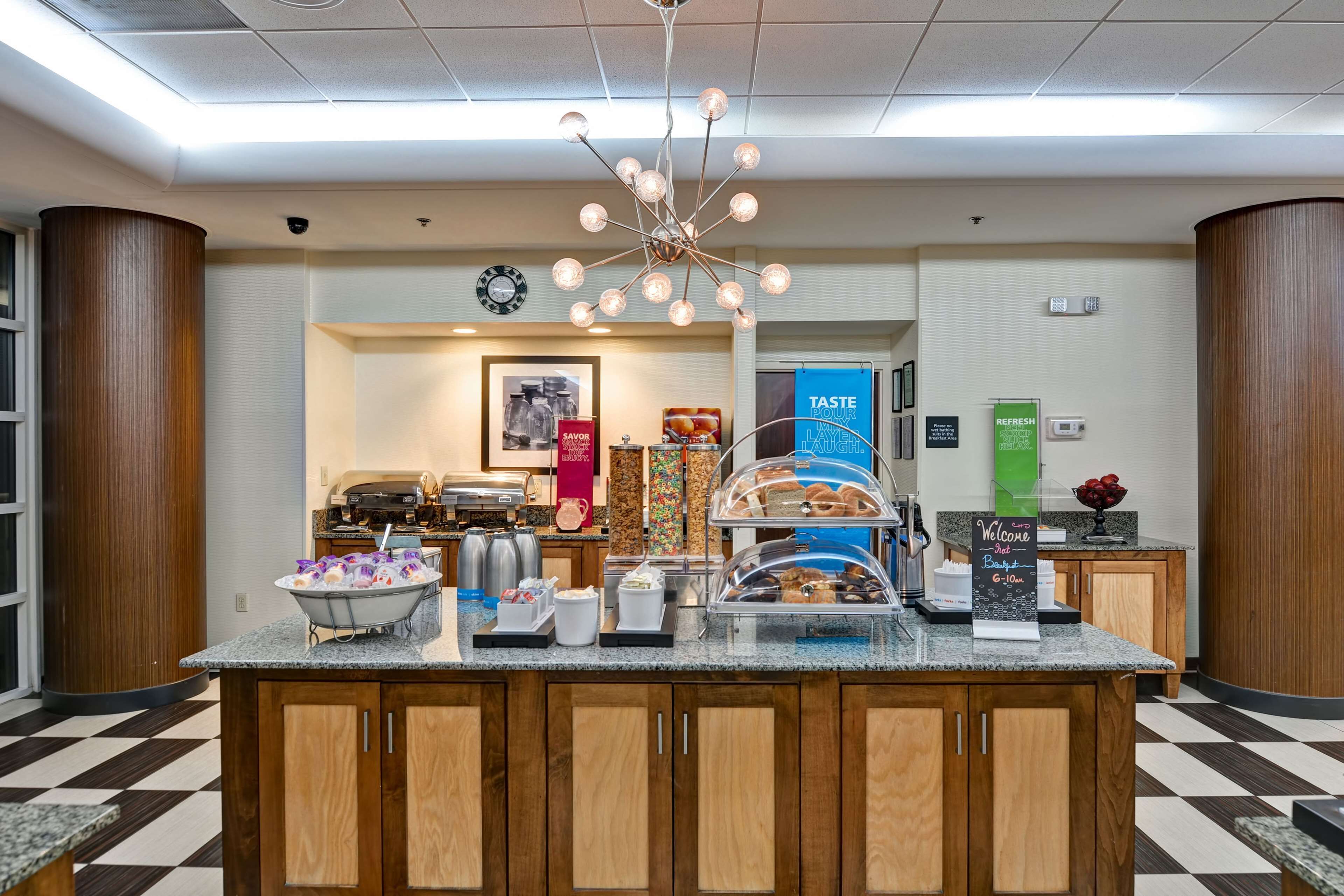 A hotel breakfast area with a central counter, coffee machines, and a variety of food items.