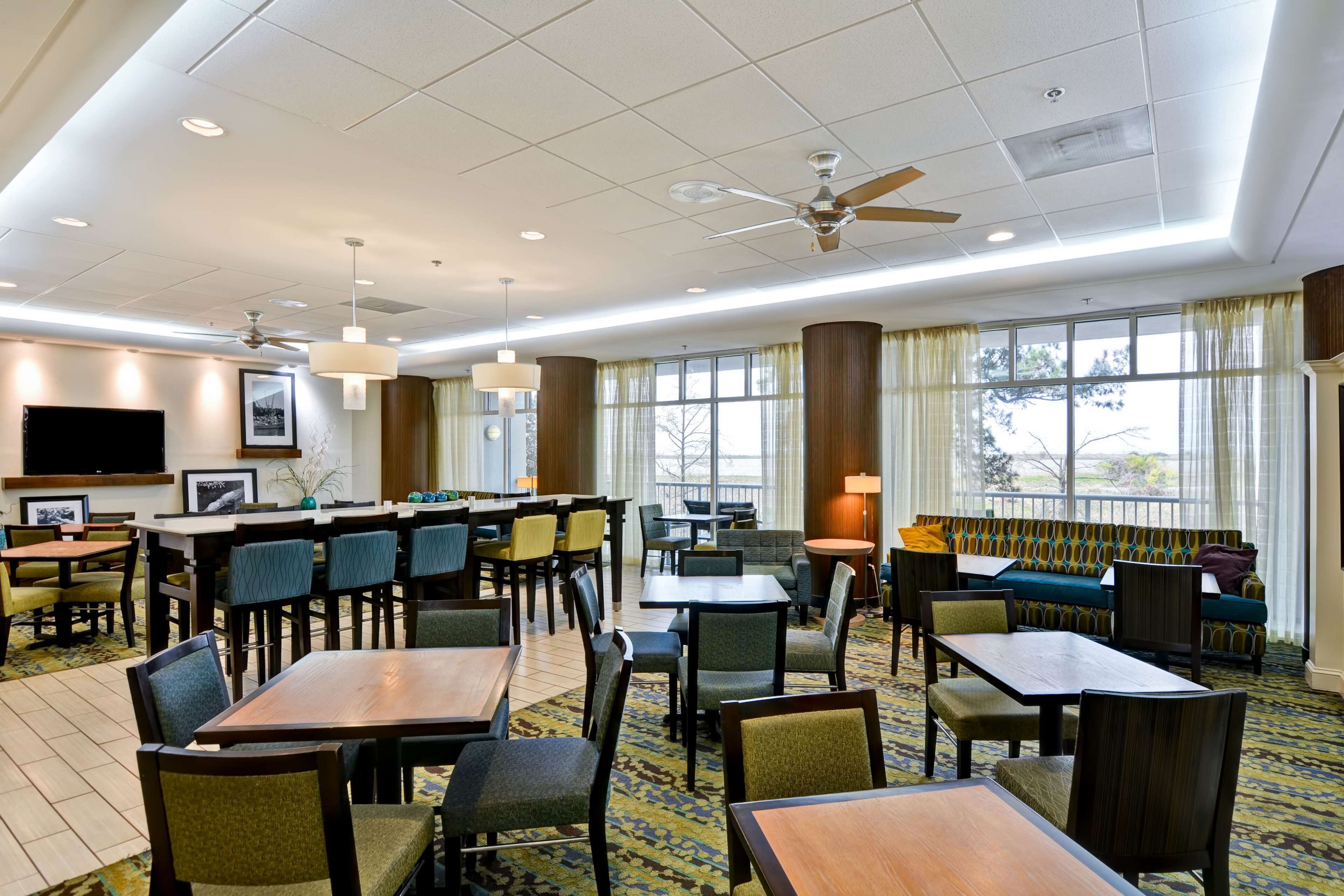 A hotel lobby with multiple dining tables, chairs, a sofa, and a TV mounted on the wall.