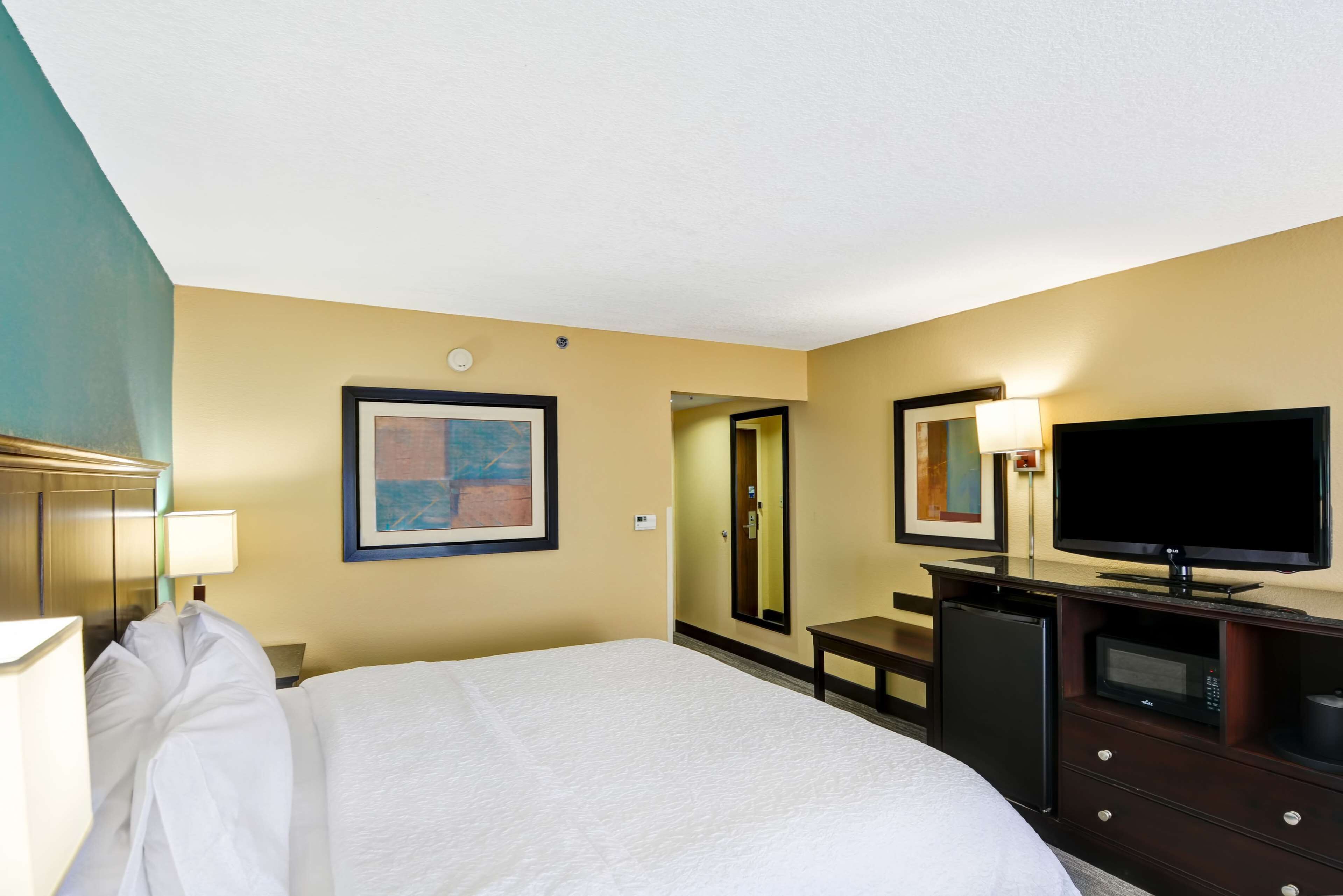 Habitación de hotel con cama, televisión, escritorio con lámpara, microondas y un cuadro en la pared.