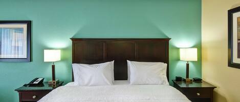 A hotel room with a large bed, two bedside tables with lamps, a telephone, and a framed picture on the wall.
