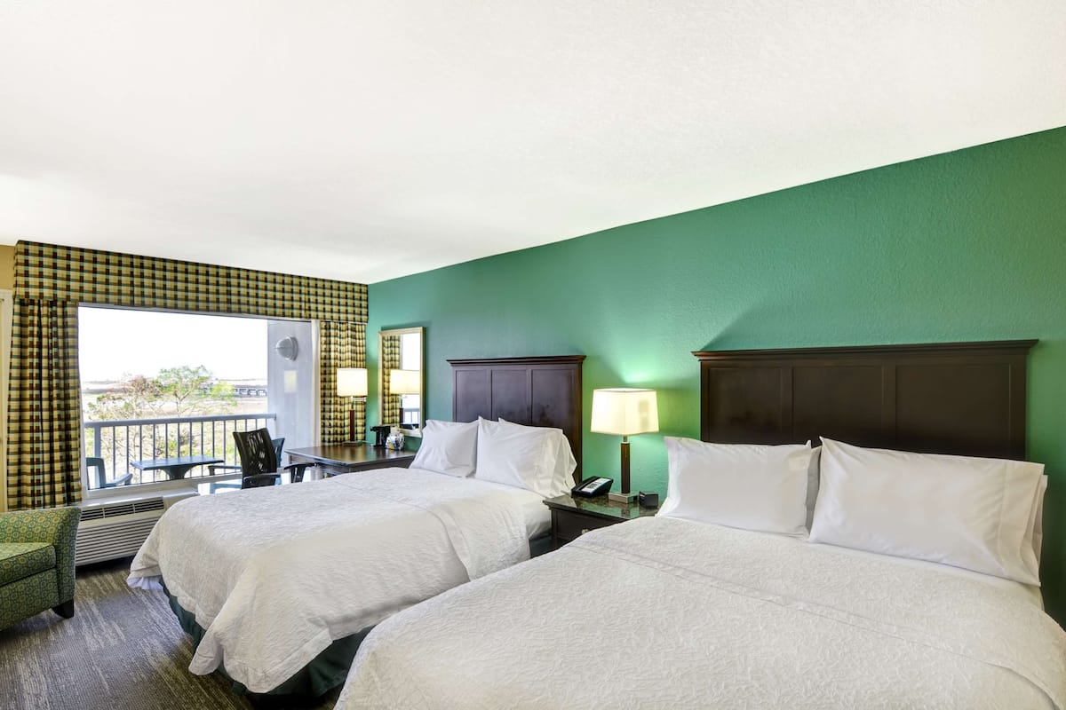 A hotel room with two beds, a balcony, a desk, and a chair.