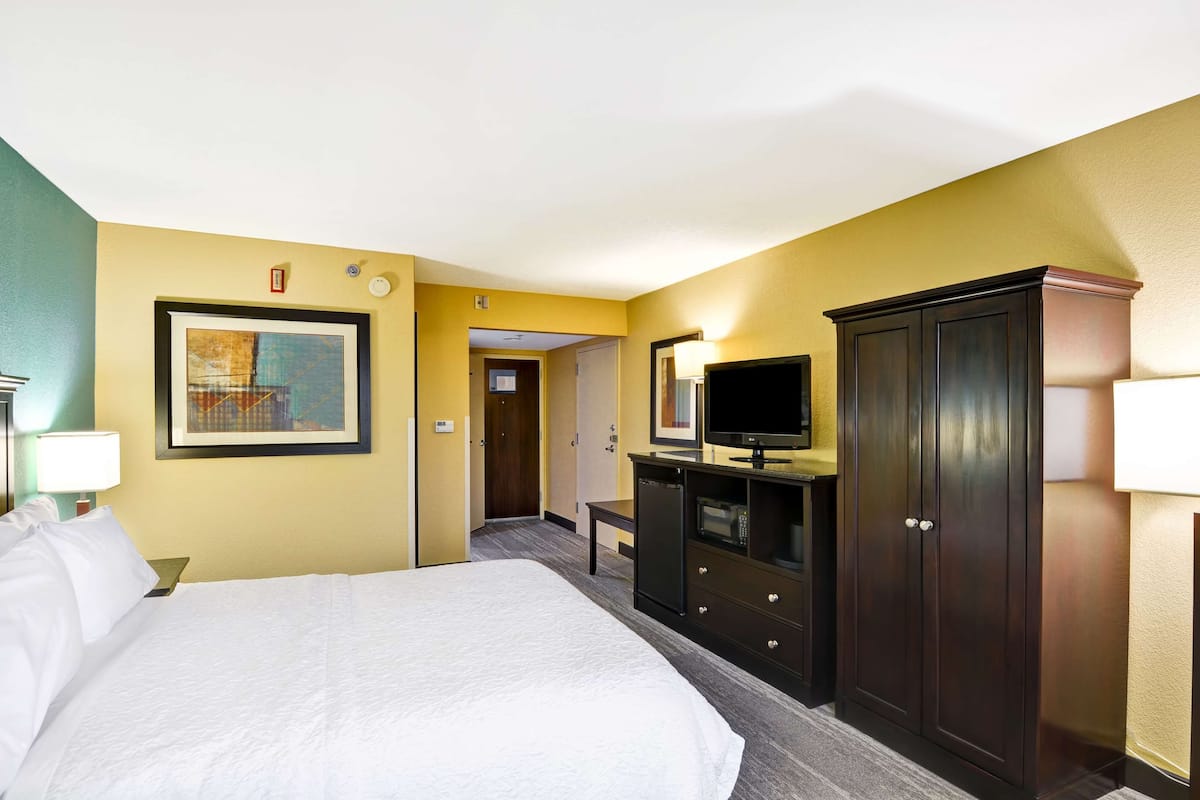 A hotel room with a large bed, a television on a dresser, a wardrobe, and a framed picture on the wall.