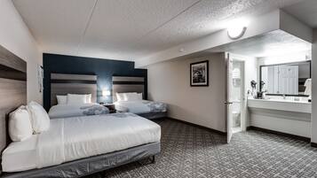 Habitación de hotel con dos camas, un espejo grande, baño con lavamanos e inodoro, y alfombra estampada.