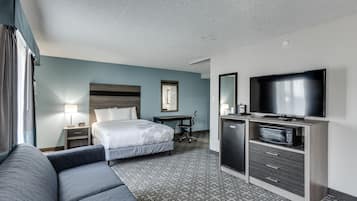 A hotel room with a bed, a sofa, a desk, a television, and a microwave.