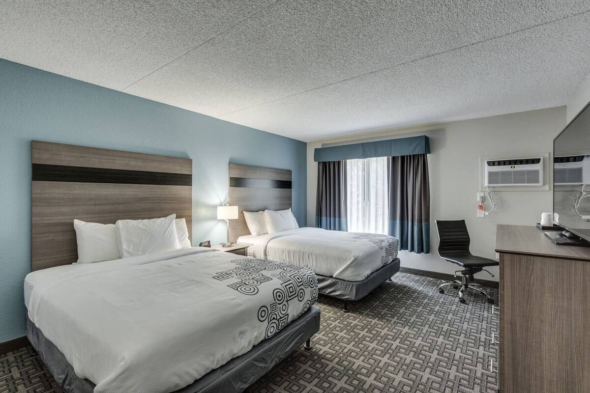A hotel room with two beds, a desk, a chair, a lamp, and a window with curtains.