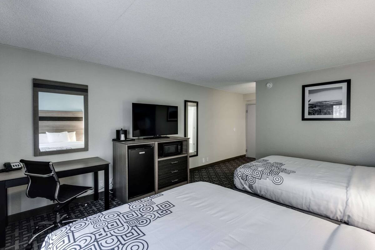A hotel room with two beds, a desk with a chair, a television, and a small cabinet.