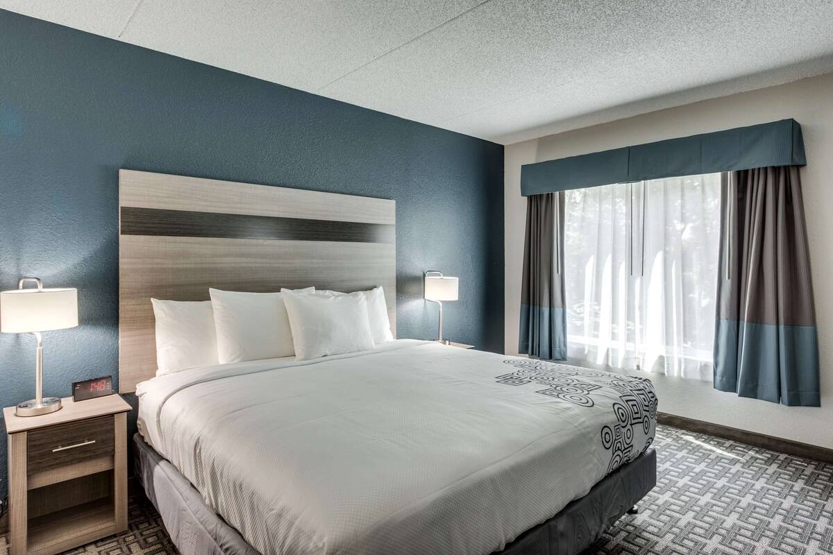 A hotel room with a large bed, two bedside tables with lamps, a headboard, and a window with curtains.