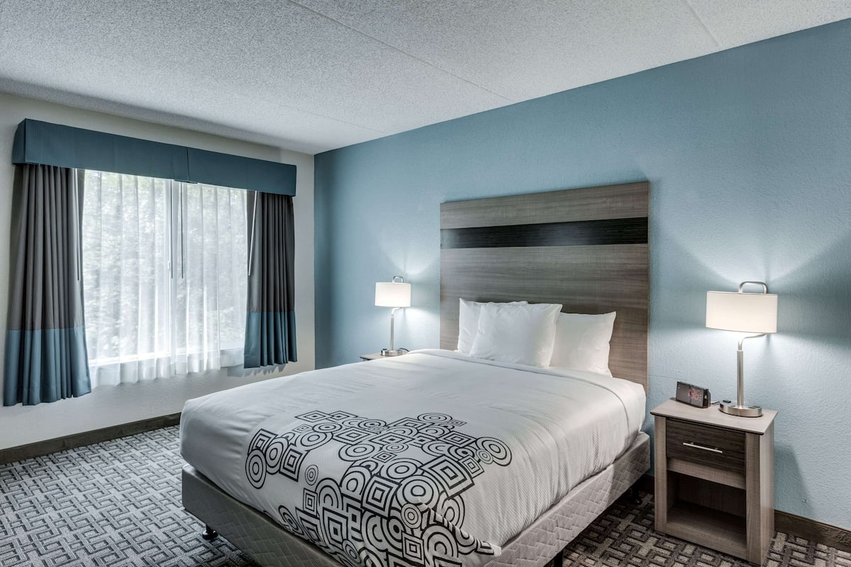 A hotel room with a large bed, two bedside lamps, a nightstand, and a window with curtains.