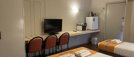 A hotel room with a desk, a television, a refrigerator, two beds with towels, and a ceiling fan.