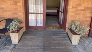 A wooden deck leading to a room with a bed and a window with floral curtains. - Philadelphia Motor Inn Echuca (Echuca)