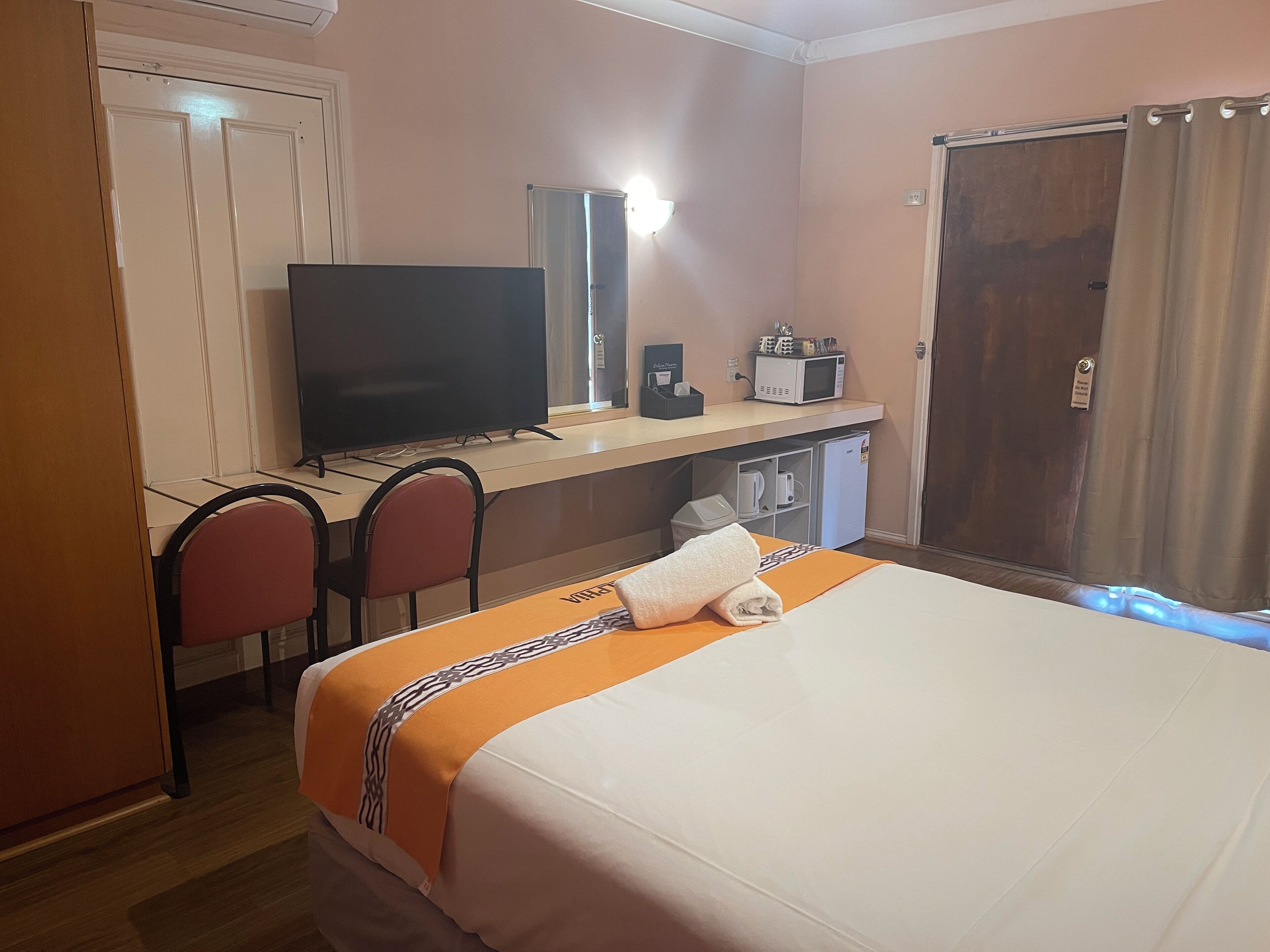 A hotel room with a bed, a desk with a TV, a microwave, and a mini-fridge.