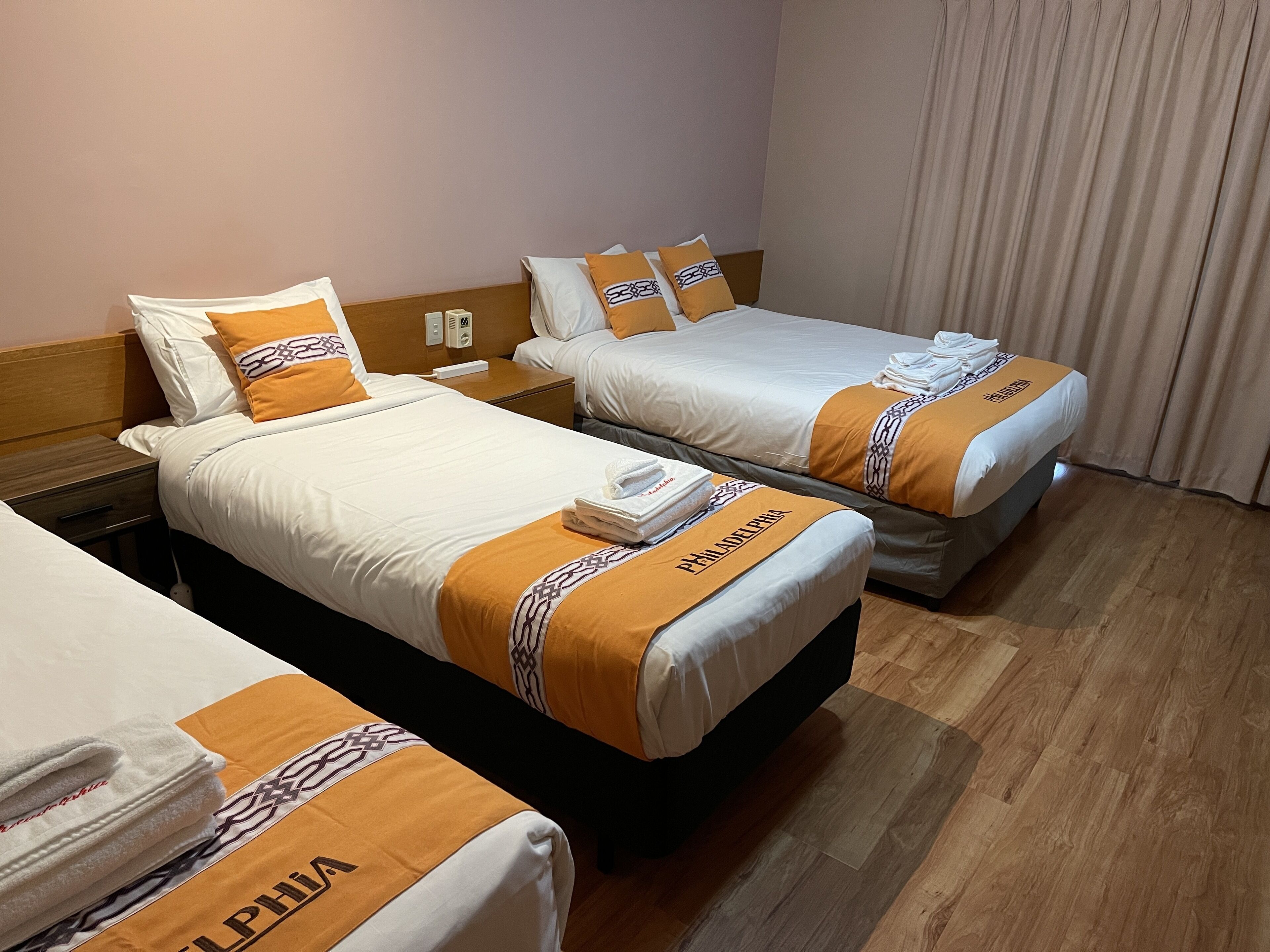 Dos camas individuales con ropa de cama blanca y naranja, un cabecero de madera y suelo de madera.