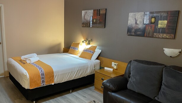 A hotel room with a bed, a nightstand, a leather sofa, and two paintings on the wall. - Philadelphia Motor Inn Echuca (Echuca)