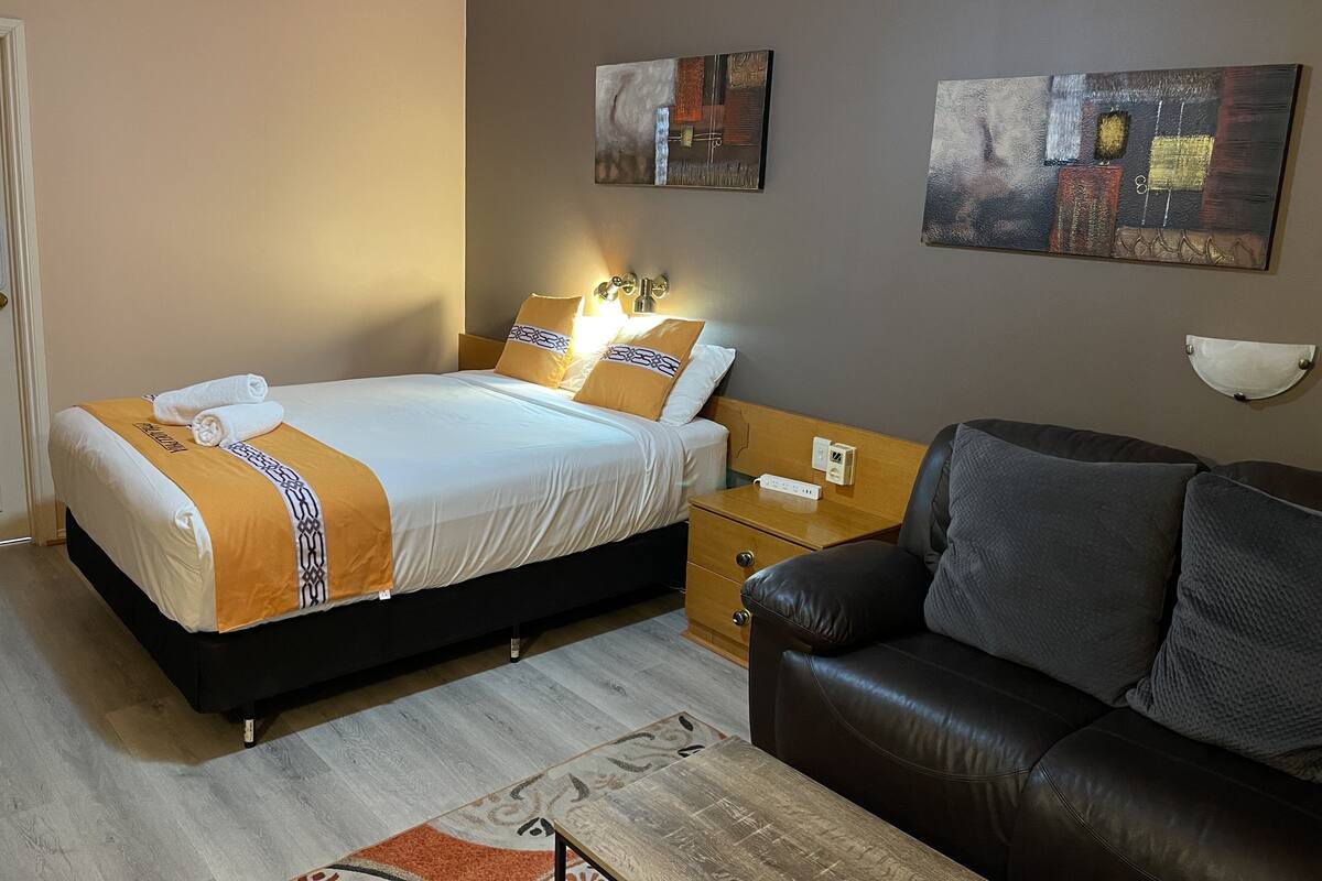 A hotel room with a bed, a nightstand, a leather sofa, and two paintings on the wall.