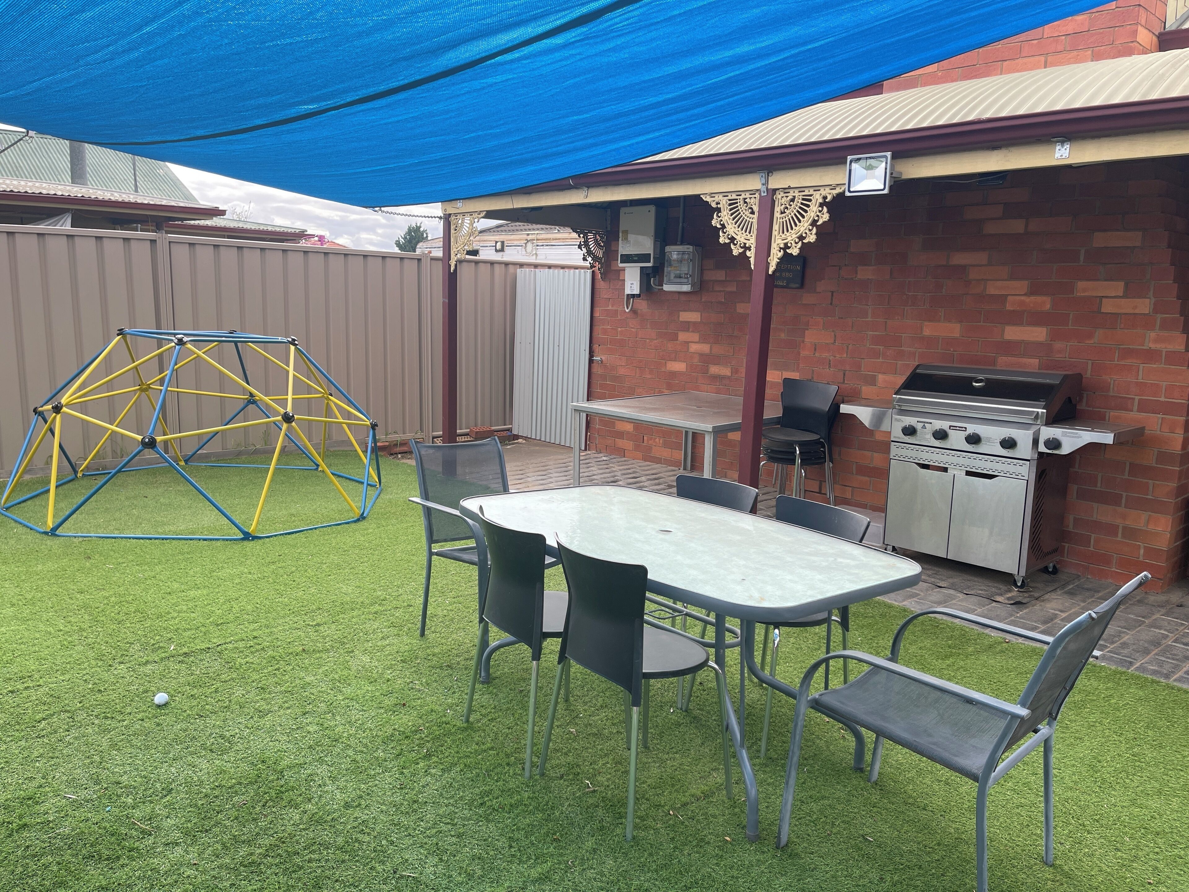 A backyard with a barbecue grill, a table with chairs, a swing set, and a covered patio area.