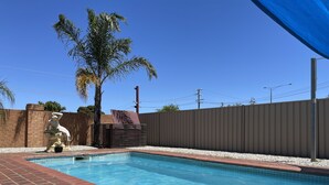 A swimming pool with a tiled edge, a palm tree, and a statue. - Philadelphia Motor Inn Echuca (Echuca)