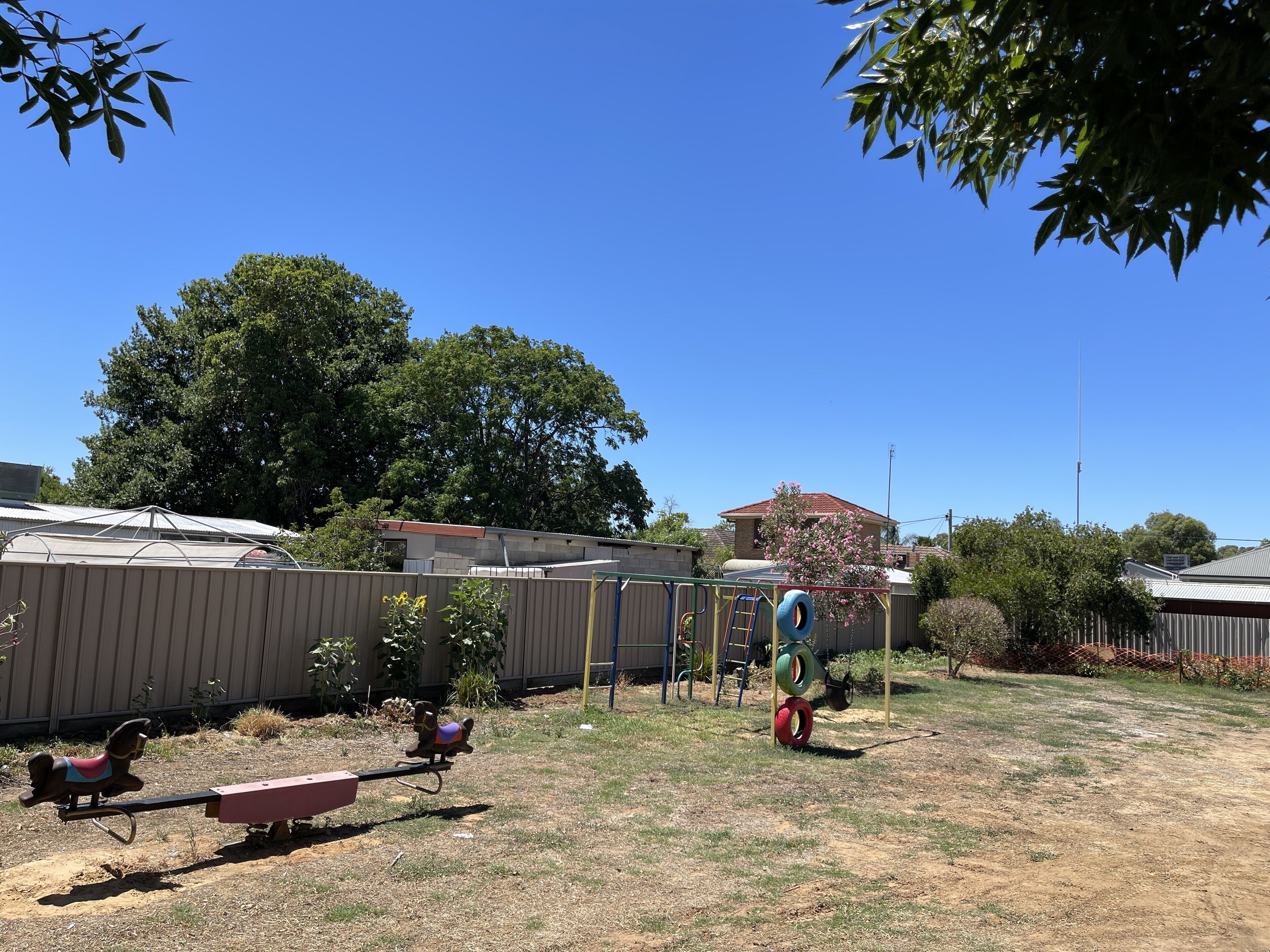 A backyard with a swing set, a seesaw, and a tire swing.
