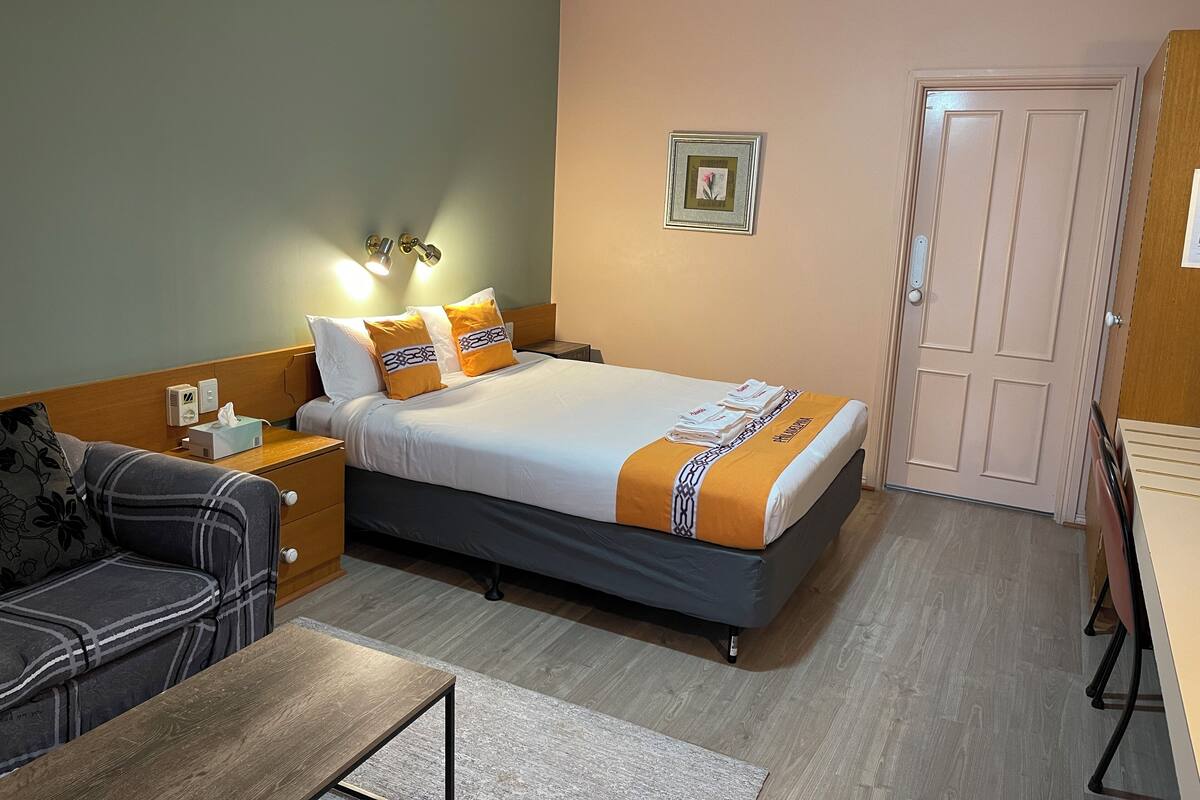 A hotel room with a bed, bedside table, lamp, and a couch.
