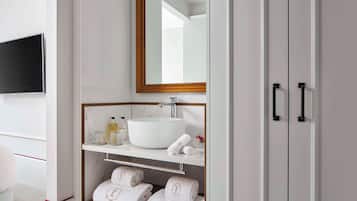 A bathroom with a large mirror, a white sink, a shelf with toiletries, and a towel rack with towels.